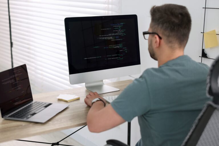 Mężczyzna pracujący przy biurku z komputerem i laptopem.