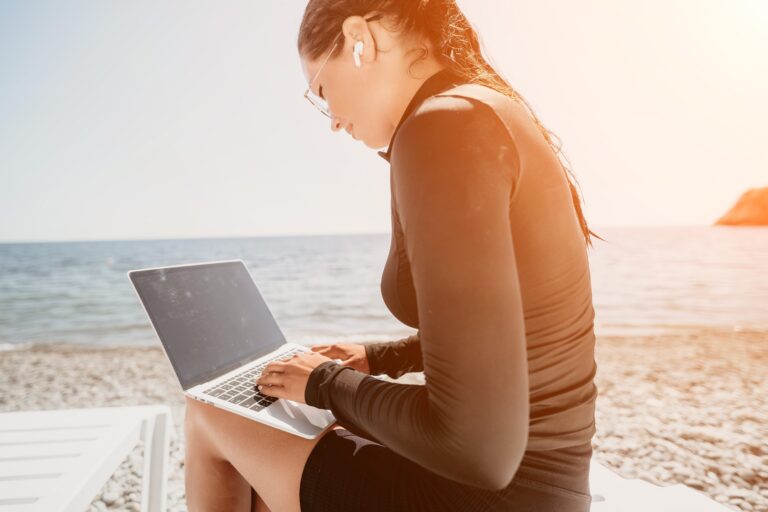 Kobieta w słuchawkach bezprzewodowych korzystająca z laptopa na plaży.