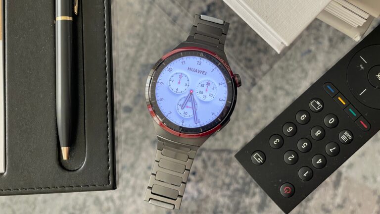 Smartwatch Huawei z metalową bransoletą, długopis oraz pilot do telewizora na stole.