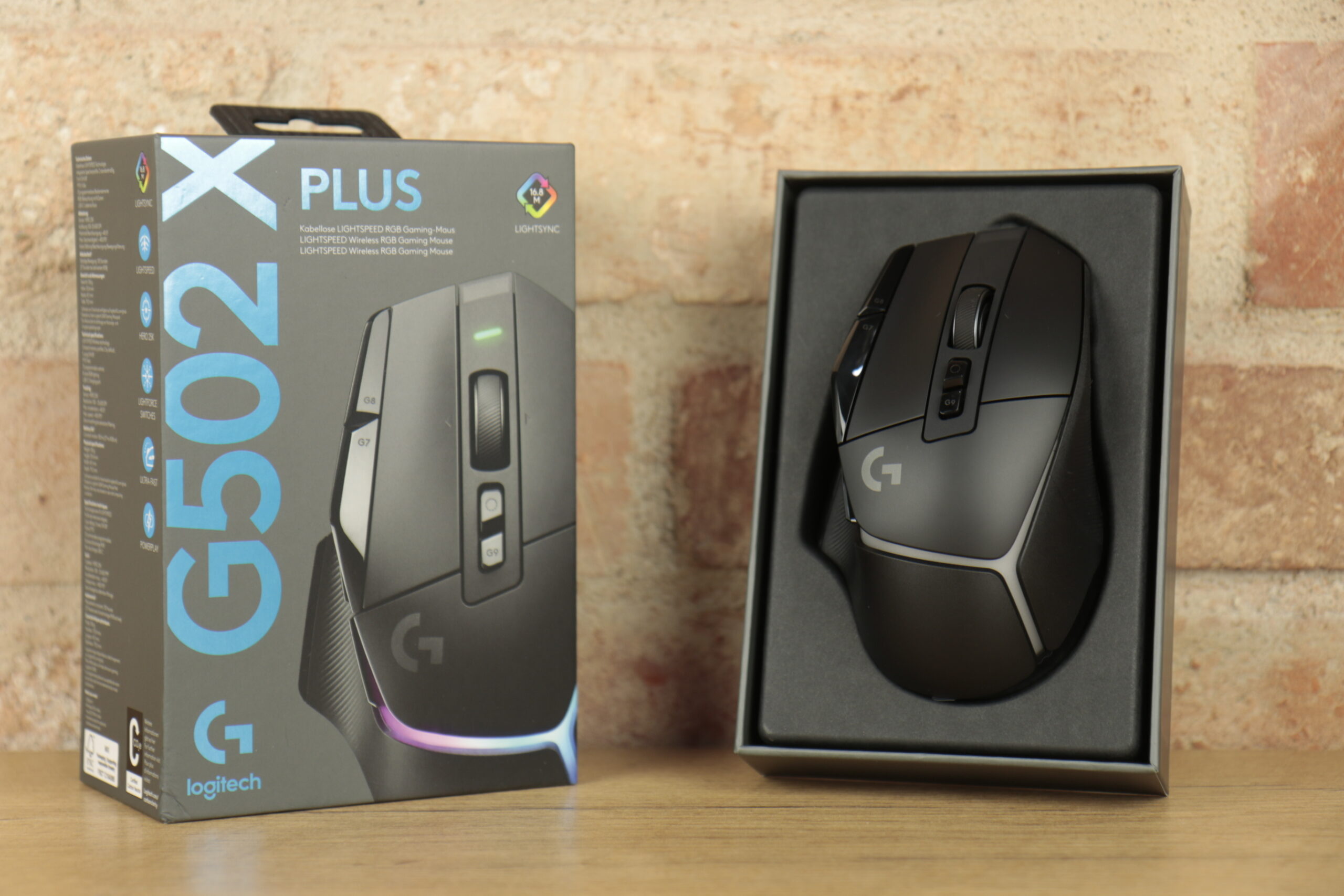 Recenzja Logitech G502 X Plus - bezprzewodowa mysz gamingowa w pudełku na drewnianym stole.