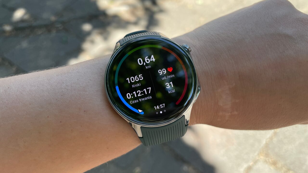 Smartwatch na nadgarstku z wyświetlaczem pokazującym: 0,64 km, 1065 kroków, 99 uderzeń na minutę, czas trwania 0:12:17, 31 kcal, godzina 14:57.