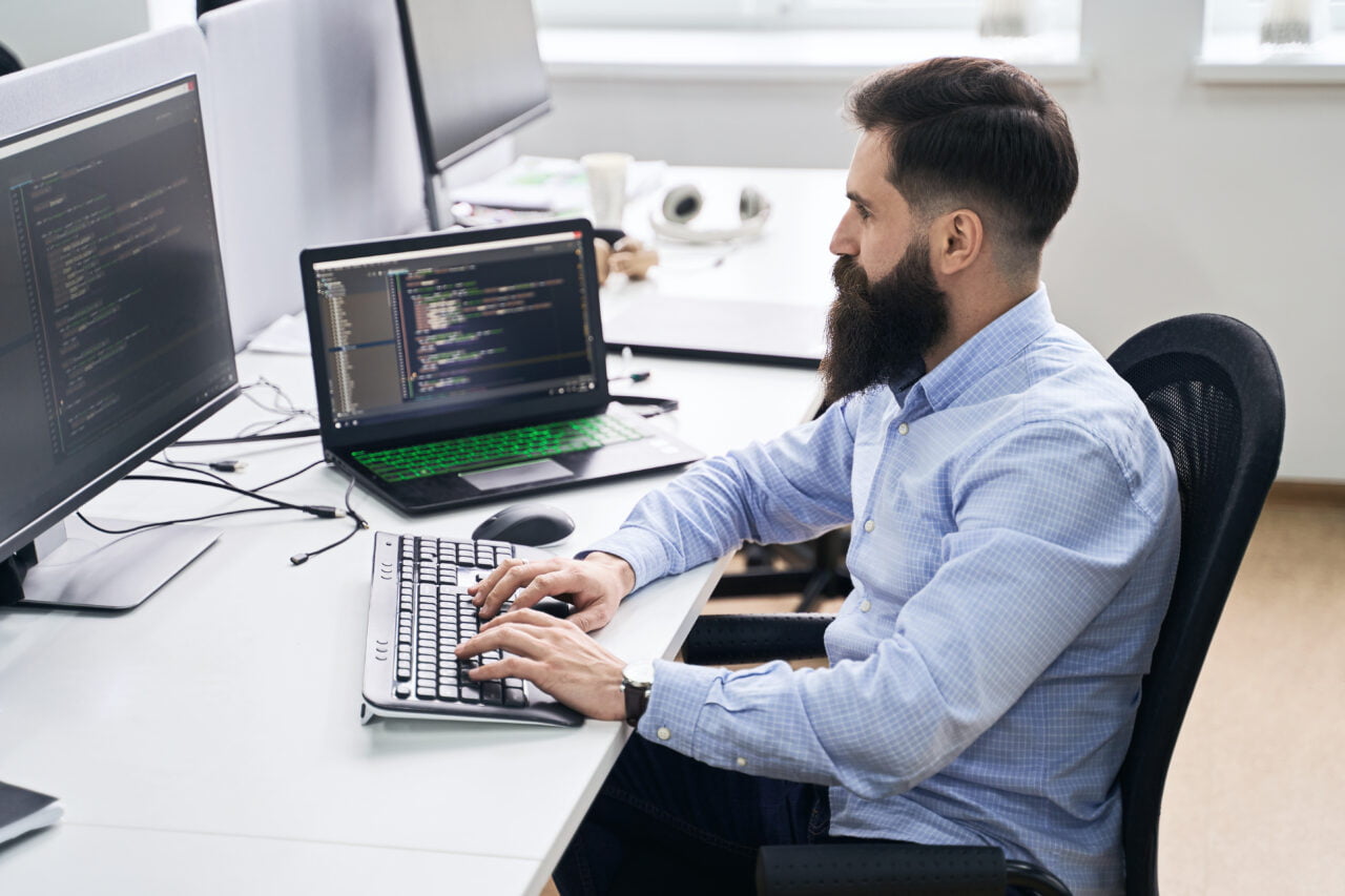 Mężczyzna pracujący przy komputerze z językiem Python, piszący kod na dwóch ekranach w biurze.