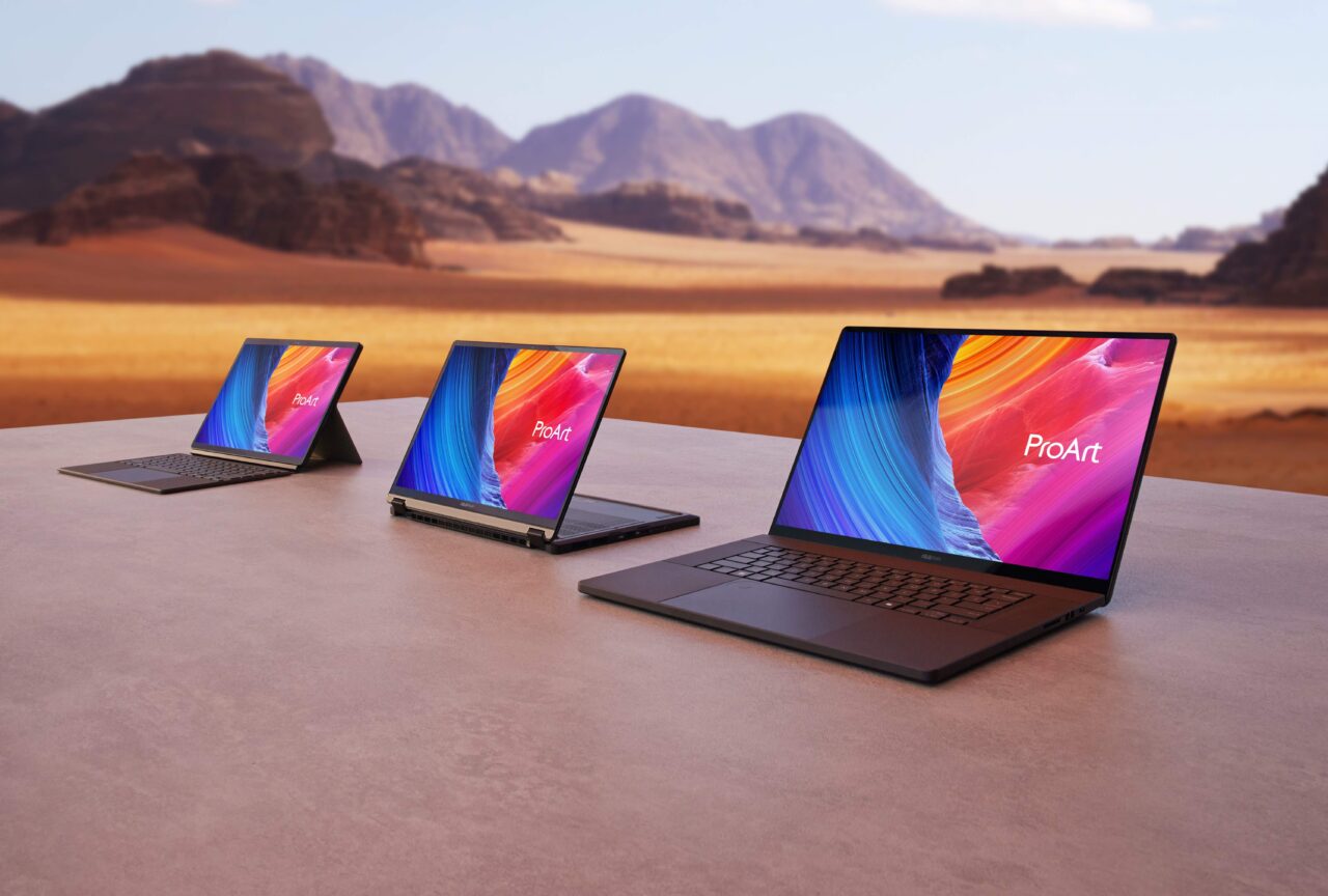 Trzy laptopy z serii ProArt stojące na stole, na tle pustynnego krajobrazu z górami w oddali.