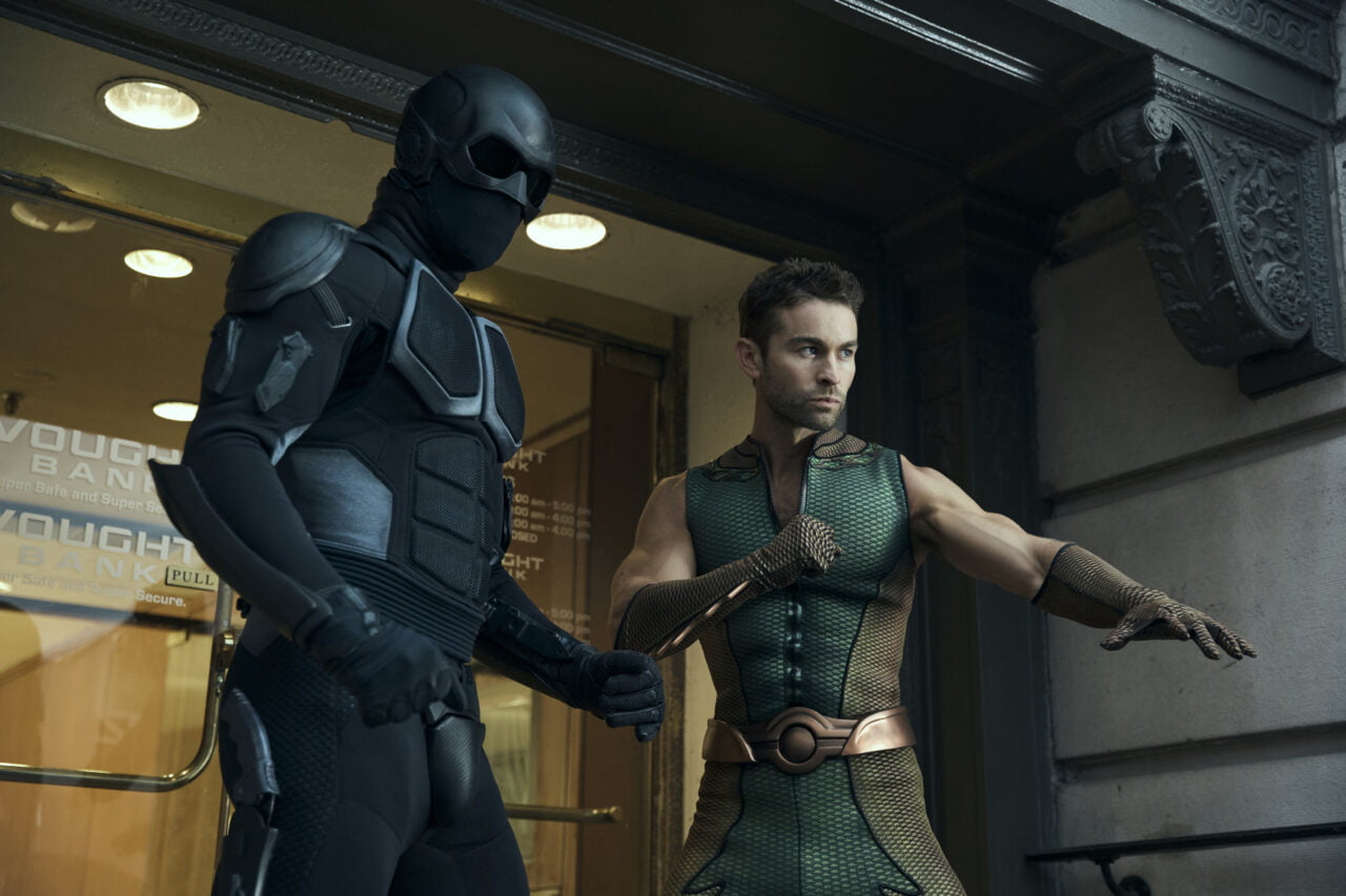 Dwóch mężczyzn w kostiumach superbohaterów stoi obok siebie na tle budynku.