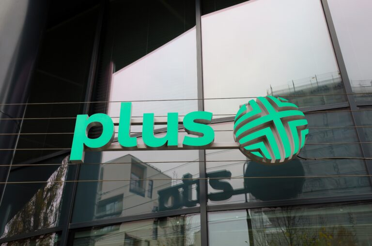 Zielone logo Plus na szklanym budynku.