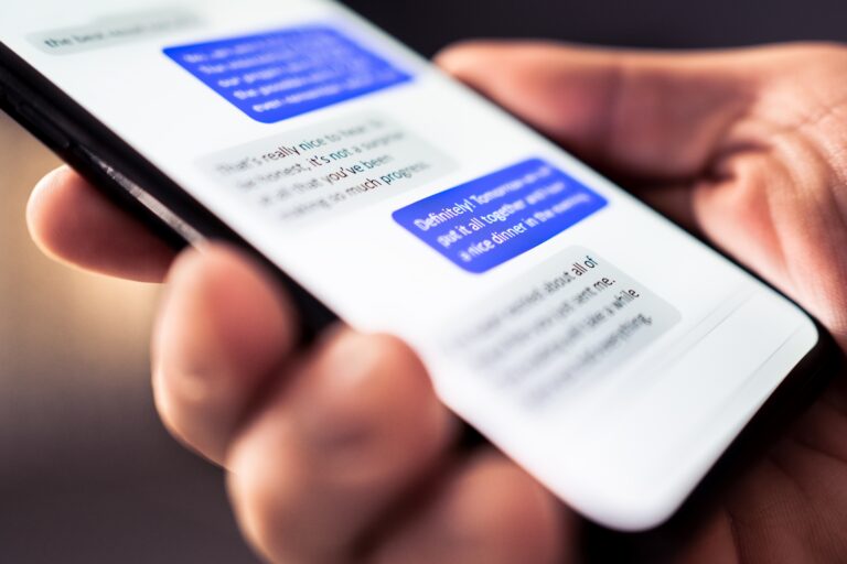 Osoba trzymająca smartfon z widoczną na ekranie aplikacją do wymiany wiadomości tekstowych.