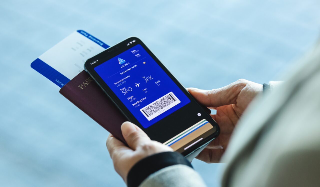 Osoba trzymająca telefon z cyfrową kartą pokładową, paszport oraz bilet lotniczy.
