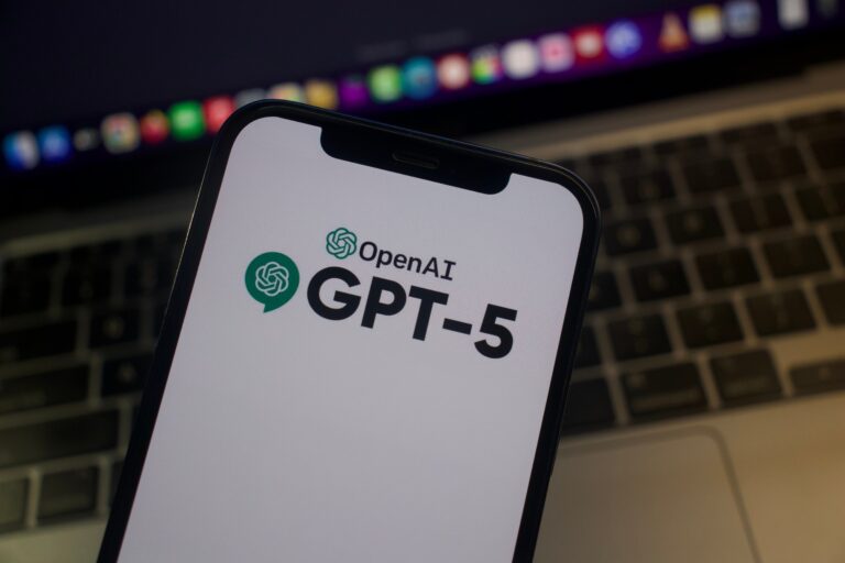 Ekran telefonu z logo OpenAI GPT-5 na tle klawiatury laptopa.