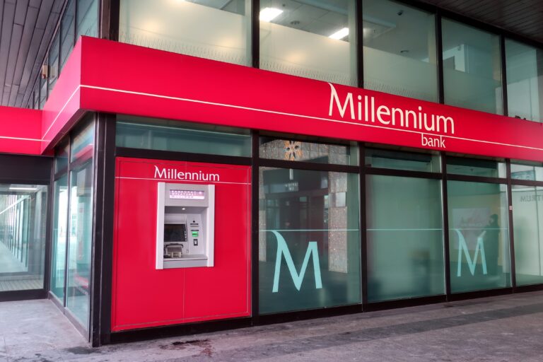 Bank Millennium z bankomatem, czerwone szyldy i przeszklone ściany.