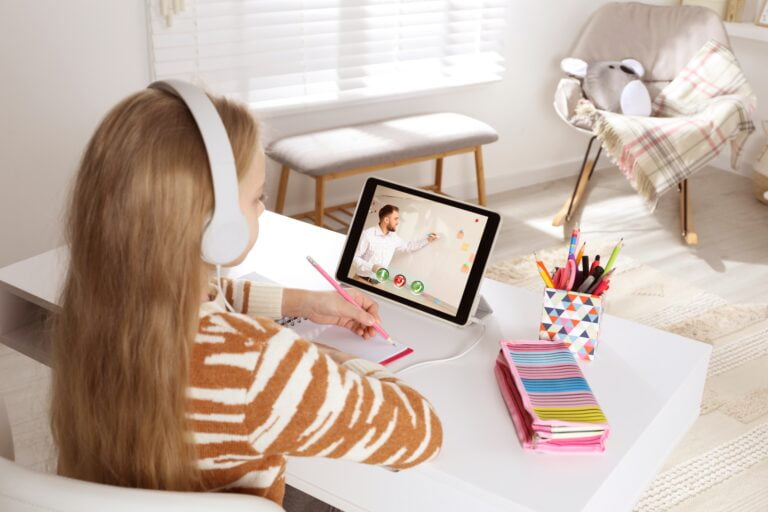 Dziecko w słuchawkach uczestniczy w lekcji online na tablecie, siedząc przy biurku w jasnym pokoju.