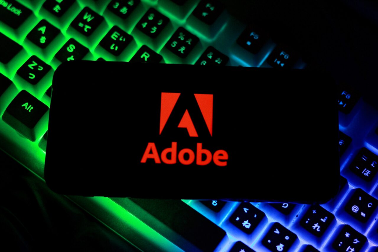Logo Adobe na tle podświetlanej klawiatury.