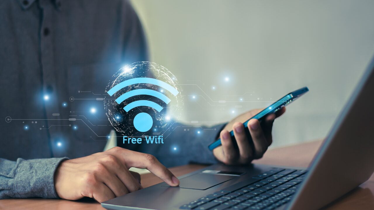 Osoba korzystająca z laptopa i smartfona, z ikoną "Free Wifi" unoszącą się nad urządzeniami.