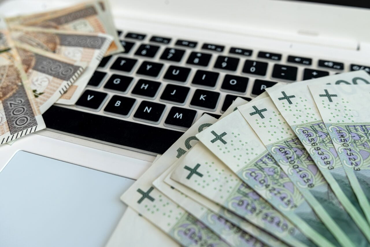 Banknoty polskich złotych na klawiaturze laptopa. Obrazek reprezentuje wysokie zarobki, którymi mogą się pochwalić programiści.
