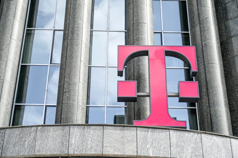 Logo T-Mobile na tle nowoczesnego budynku z przeszkloną fasadą.