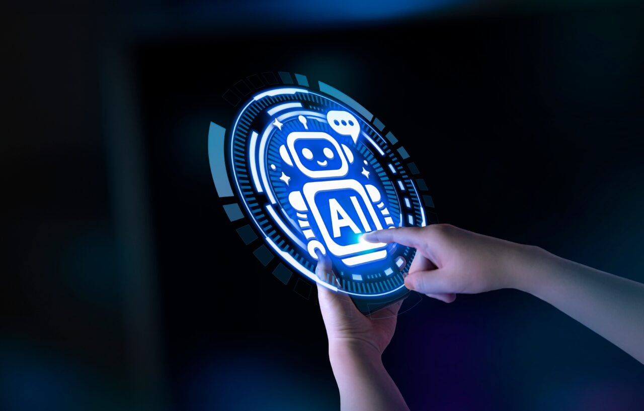 Osoba dotyka holograficznego interfejsu przedstawiającego robota z napisem "AI".