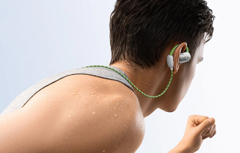 Mężczyzna z mokrymi plecami biegnie, nosząc zielone słuchawki.