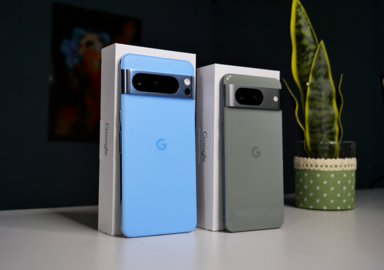 Smartfony Google Pixel 8 i 8 Pro stoją na białym blacie, są oparte o pudełka.