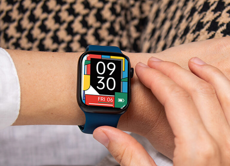Osoba nosząca smartwatch z kolorowym wyświetlaczem i niebieskim paskiem, zbliżenie na nadgarstek.