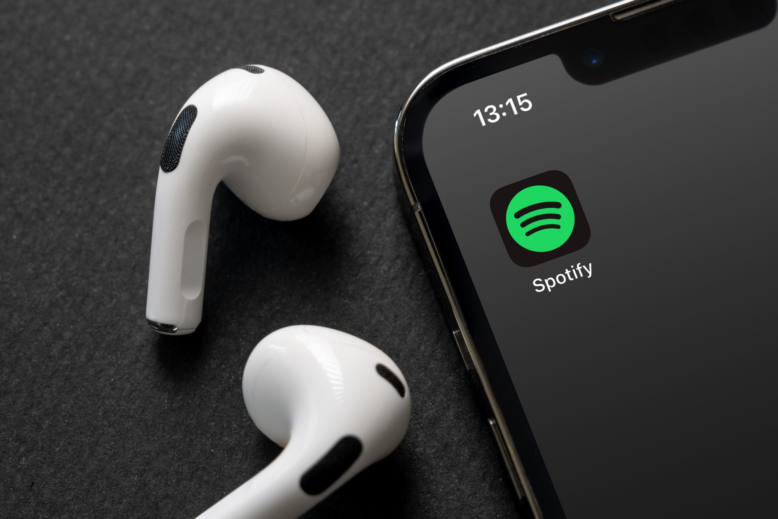 Słuchawki bezprzewodowe obok smartfona z aplikacją Spotify na ekranie.