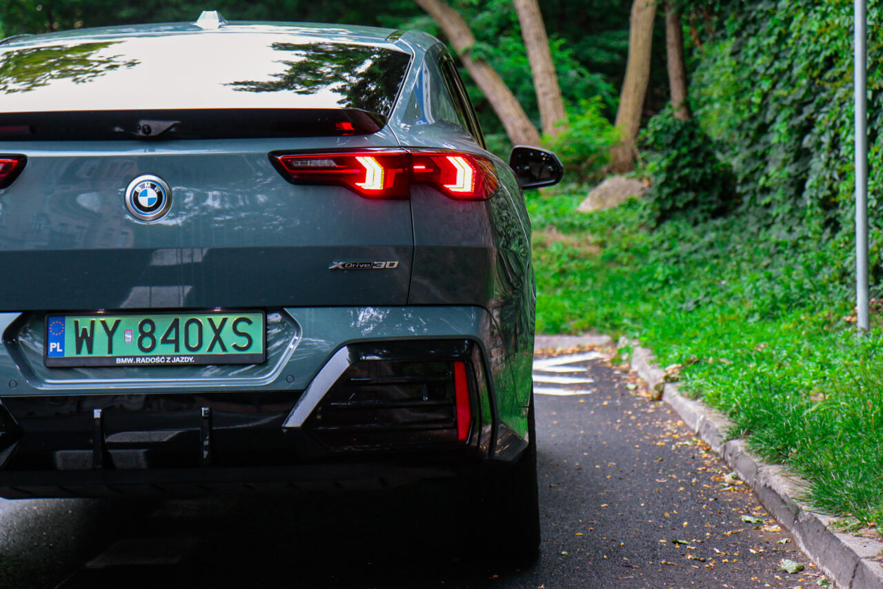 Tył samochodu BMW iX2 z widoczną tablicą rejestracyjną podczas testu w lesie.