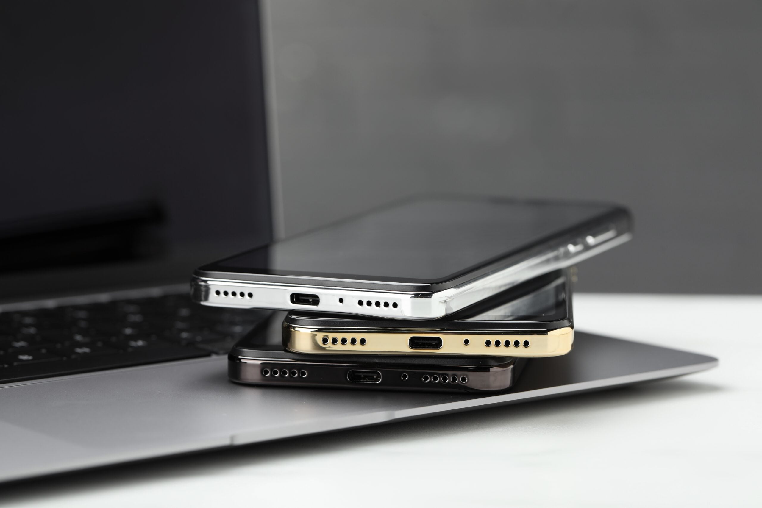 Trzy smartfony ułożone jeden na drugim, leżące na laptopie.