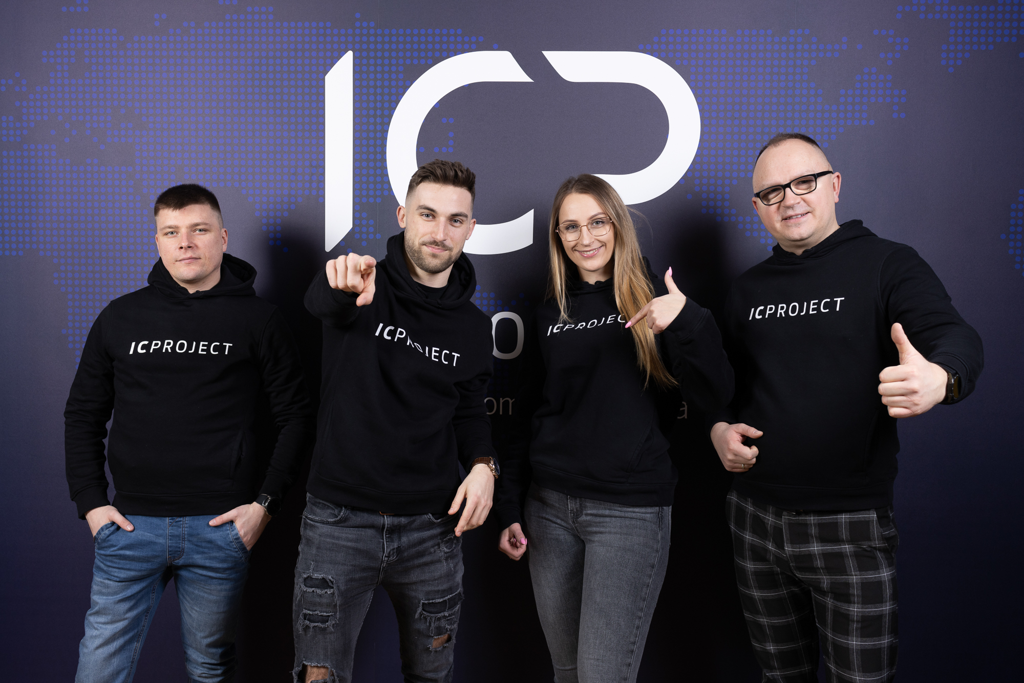 ICPROJECT. Czworo osób w czarnych bluzach z napisem "ICPROJECT" stoi na tle ciemnej ściany z dużym logo "ICP".