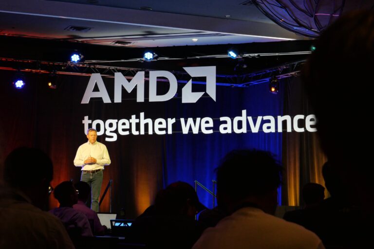 Mężczyzna stojący na scenie z logo AMD i napisem "together we advance" w tle, przed audytorium.