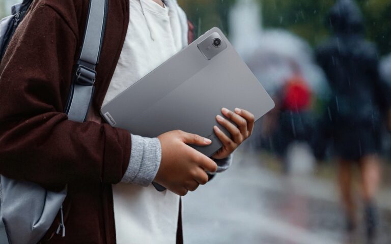 Osoba trzymająca tablet Lenovo na tle deszczowej ulicy.