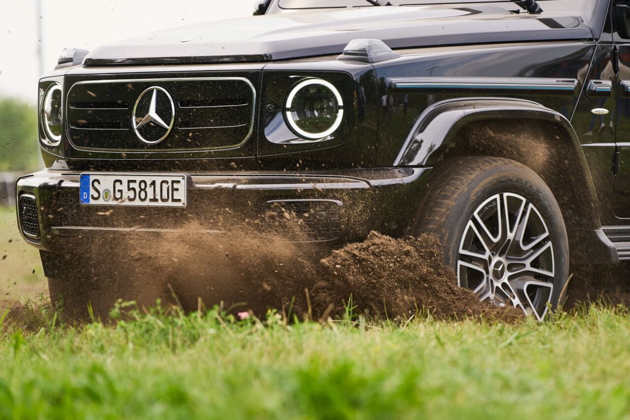 Czarny SUV Mercedes-Benz klasy G jeżdżący po błotnistej trawie.