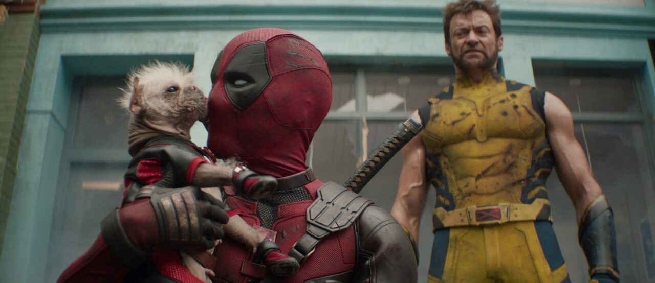 Deadpool & Wolverine kadr z filmu. Deadpool trzymający kosmitę, z Wolverine'em stojącym za nim w zniszczonym żółtym stroju.