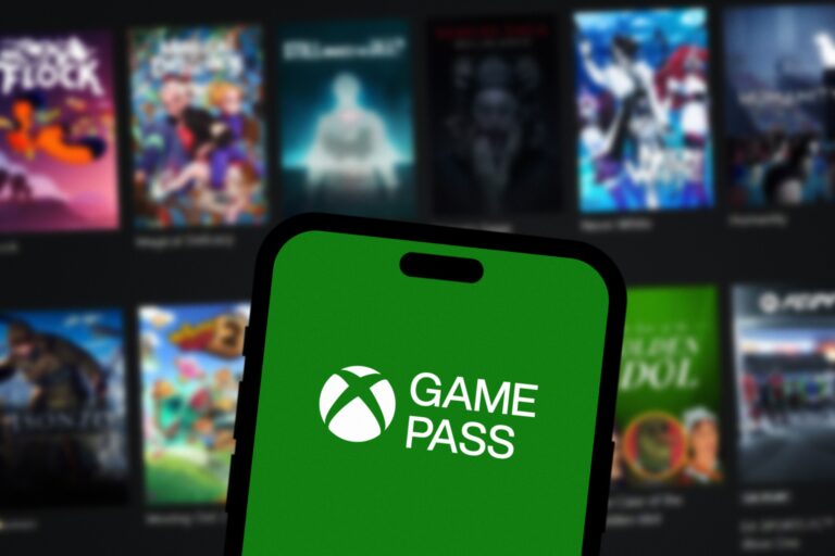 Telefon z logo Xbox Game Pass na zielonym tle, na rozmazanym tle widać okładki gier wideo.