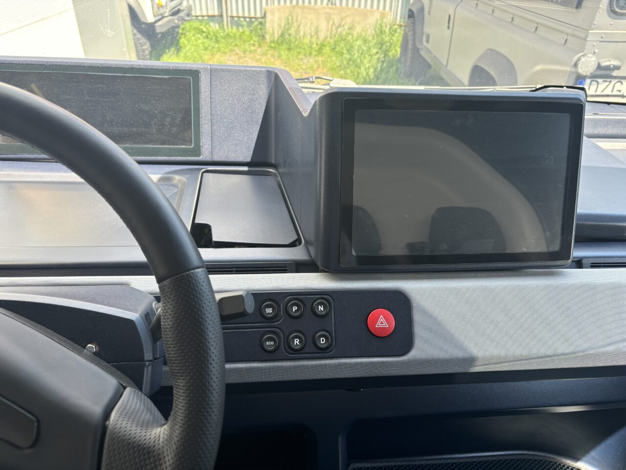 Kokpit samochodu elektrycznego z dużym ekranem dotykowym na centralnej konsoli i przyciskami kontroli jazdy.