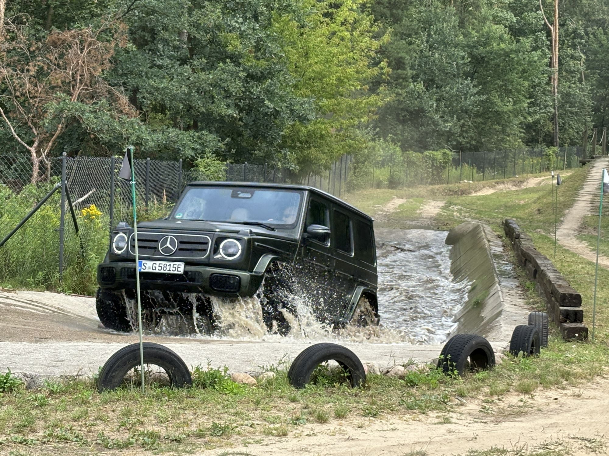 Samochód terenowy Mercedes-Benz G klasy przejeżdżający przez strumień na torze terenowym w lesie.