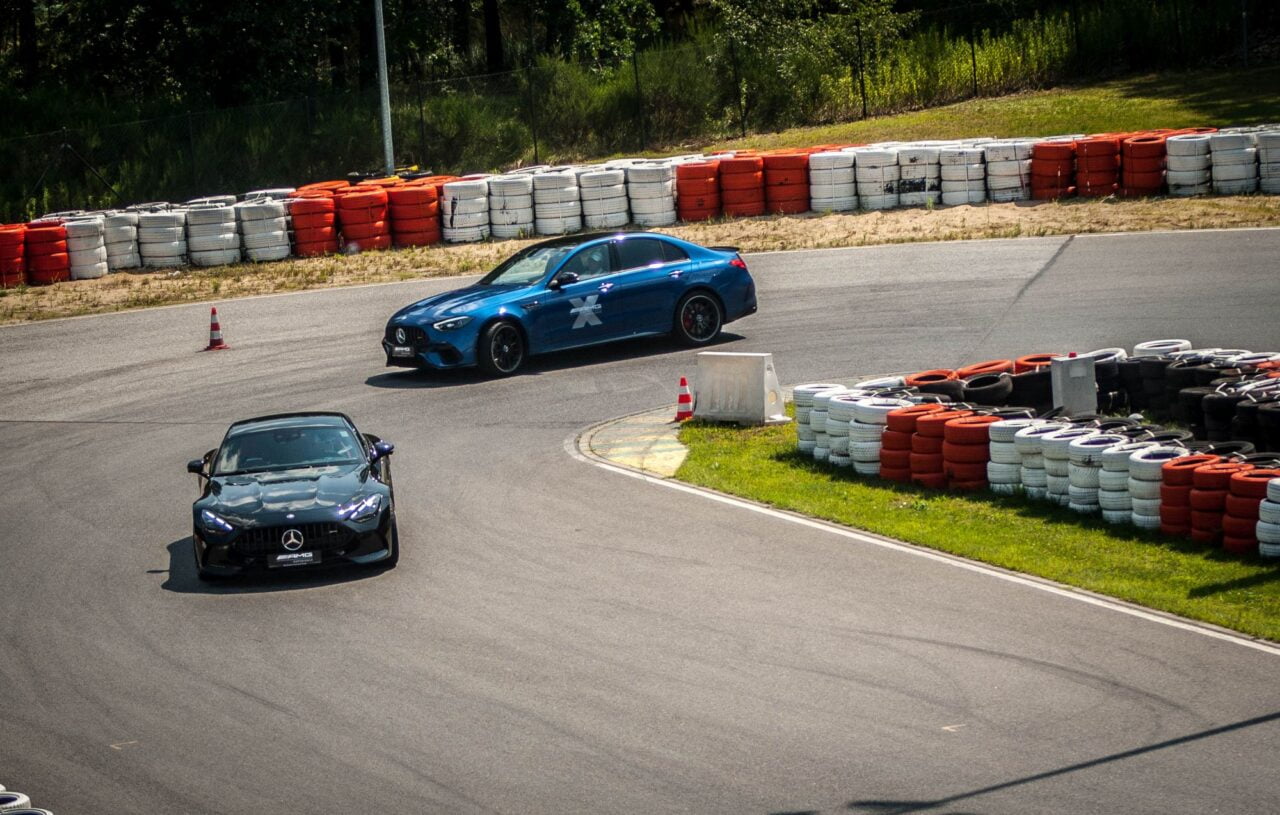 Dwa samochody sportowe Mercedes-AMG na torze wyścigowym, otoczone barierkami z opon w kolorach biało-pomarańczowych.