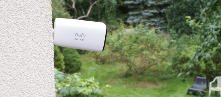 Kamera monitoringu eufy zamontowana na ścianie budynku, w tle ogród.