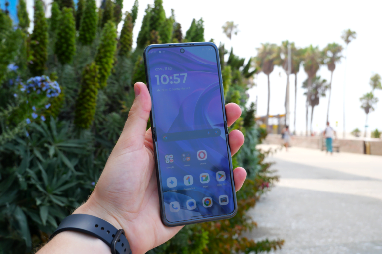 Smartfon Motorola razr 50 ultra trzymany w ręku. W tle zielony krzew i palmy.