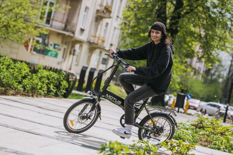 Osoba w czarnej bluzie i czapce jedzie na rowerze elektrycznym marki Motus w mieście.