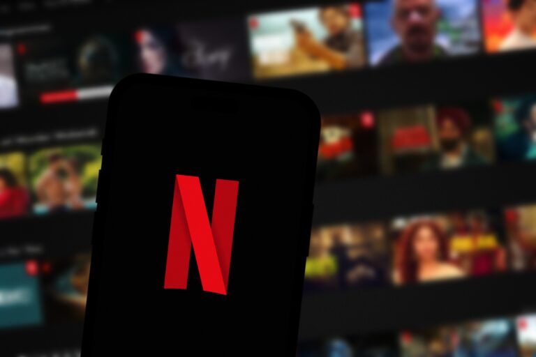 Logo Netflix na ekranie telefonu komórkowego z rozmytym tłem wideo w tle.