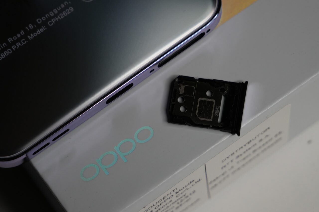 Tył smartfona Oppo z widoczną tacką na kartę SIM wyjętą obok opakowania.
