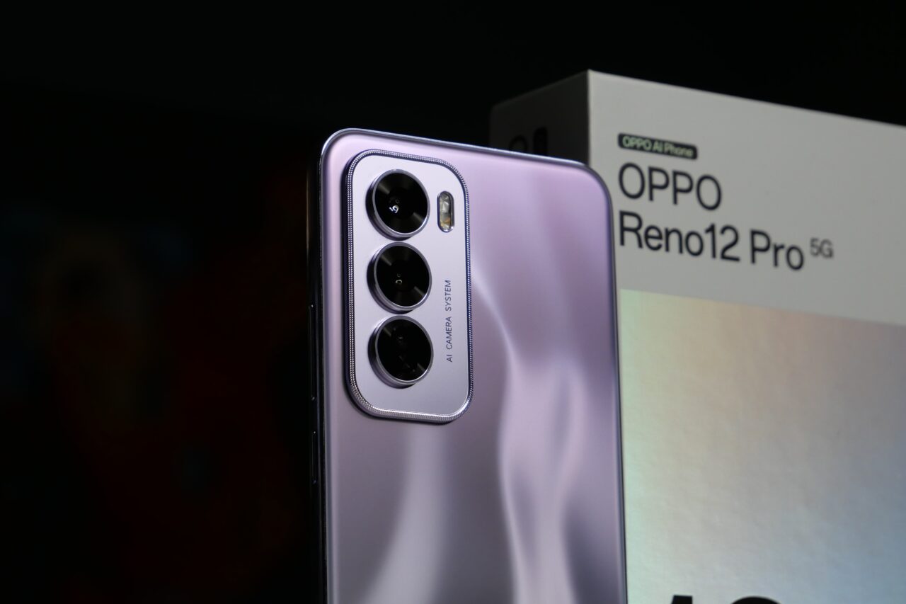 Smartfon OPPO Reno12 Pro 5G ze srebrnym połyskującym tyłem i potrójnym aparatem AI, w tle pudełko produktu.