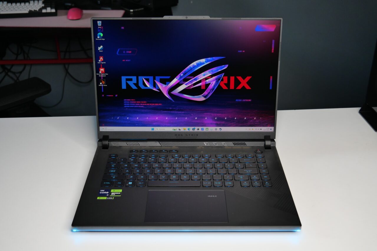 Laptop Asus ROG Strix na białym biurku, z podświetloną klawiaturą i ekranem wyświetlającym logo ROG Strix.