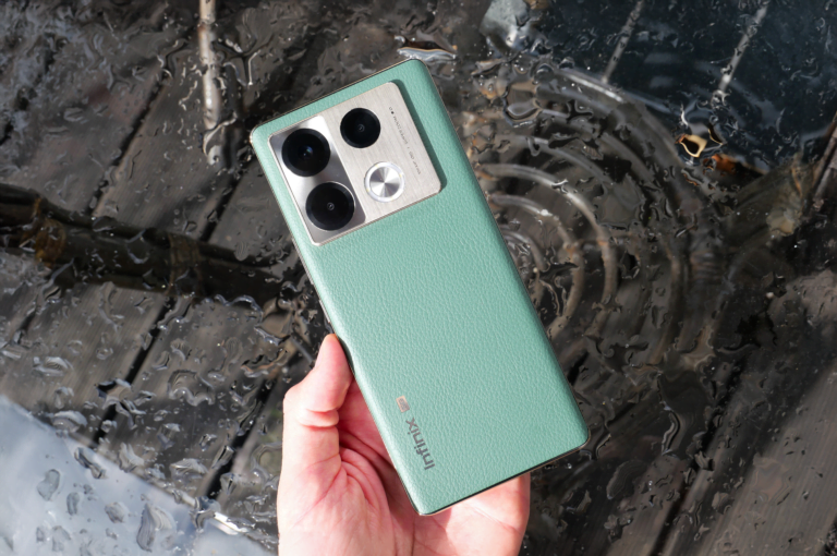 Zielony smartfon Infinix trzymany w ręce nad mokrą powierzchnią.