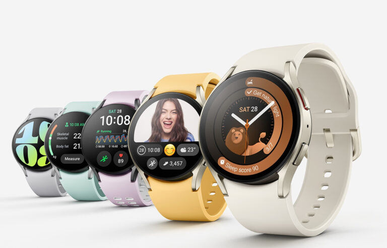 Pięć inteligentnych zegarków z kolorowymi paskami i różnymi wyświetlaczami prezentującymi różne funkcje i ekrany, ustawione w rzędzie na szarym tle.