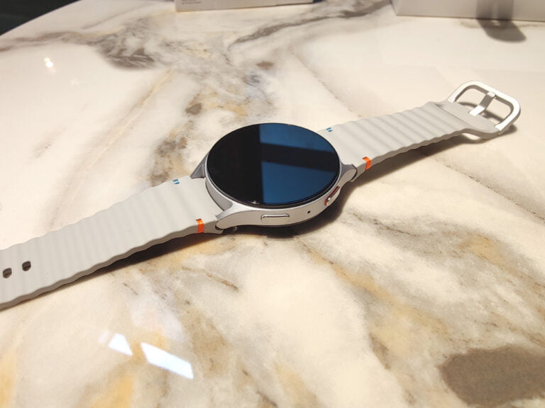 Smartwatch Samsung Galaxy Watch7 z okrągłym wyświetlaczem i szarą bransoletą, leżący na marmurowym blacie.