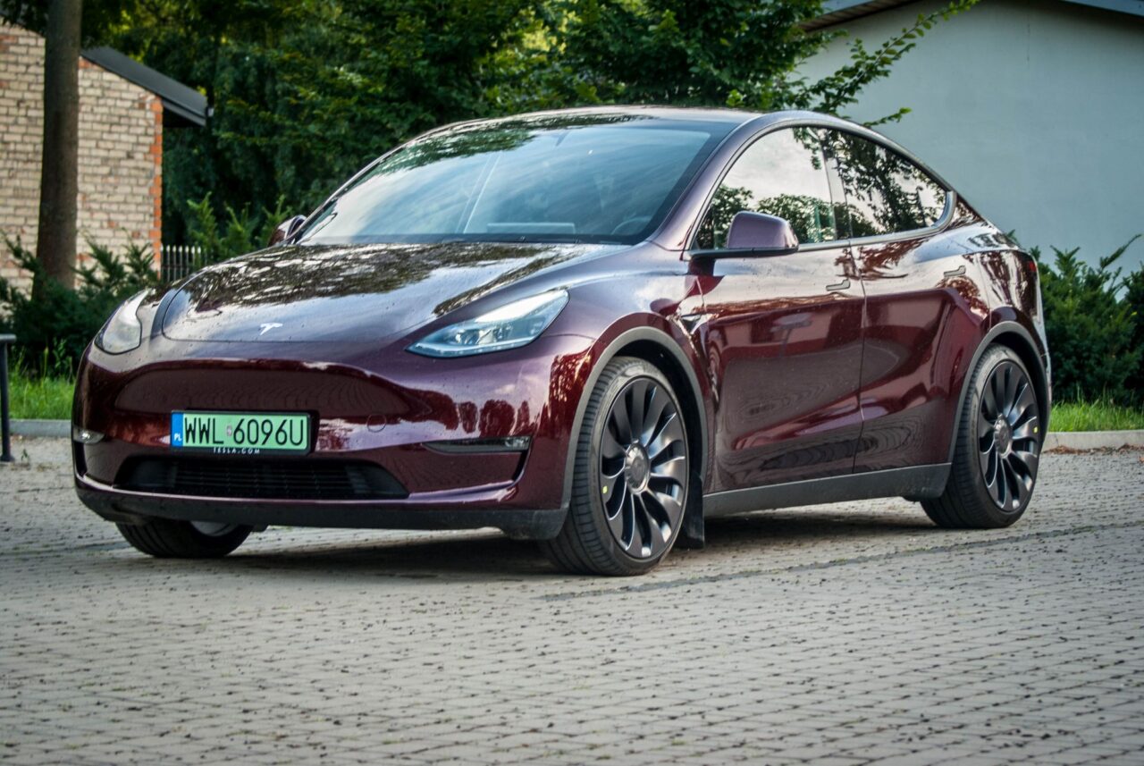 Tesla Model Y Performance w kolorze fioletowym na parkingu, widok z przodu.