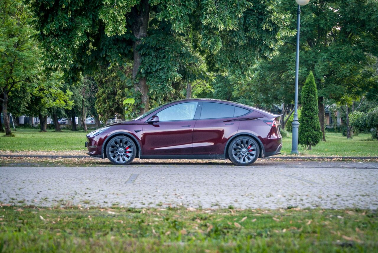 Burgundowy samochód elektryczny zaparkowany na ulicy przed parkiem.