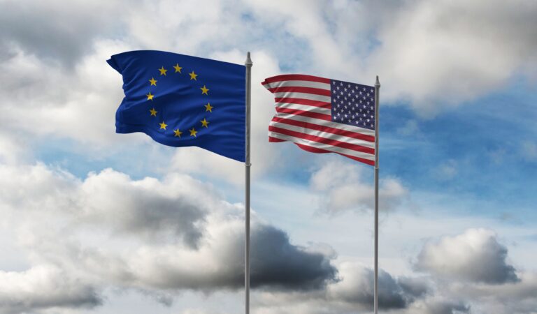 Flagi Unii Europejskiej i Stanów Zjednoczonych na masztach na tle pochmurnego nieba. Crowdstrike i Microsoft nie mają dobrego czasu z tymi instytucjami.