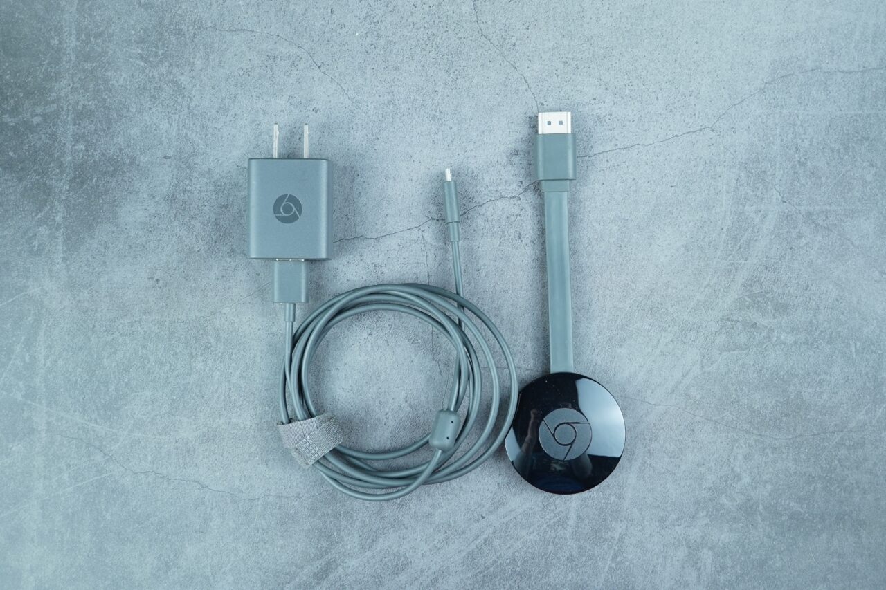 Chromecast z kablem USB i ładowarką na tle betonowej powierzchni.