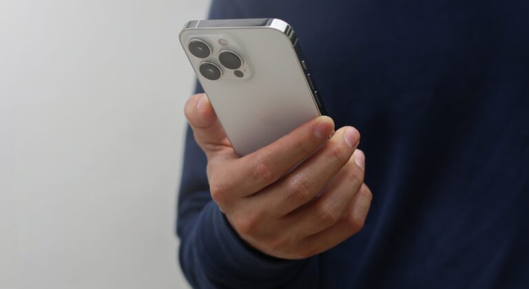 Osoba trzymająca w ręku srebrny smartfon z trzema obiektywami aparatu.