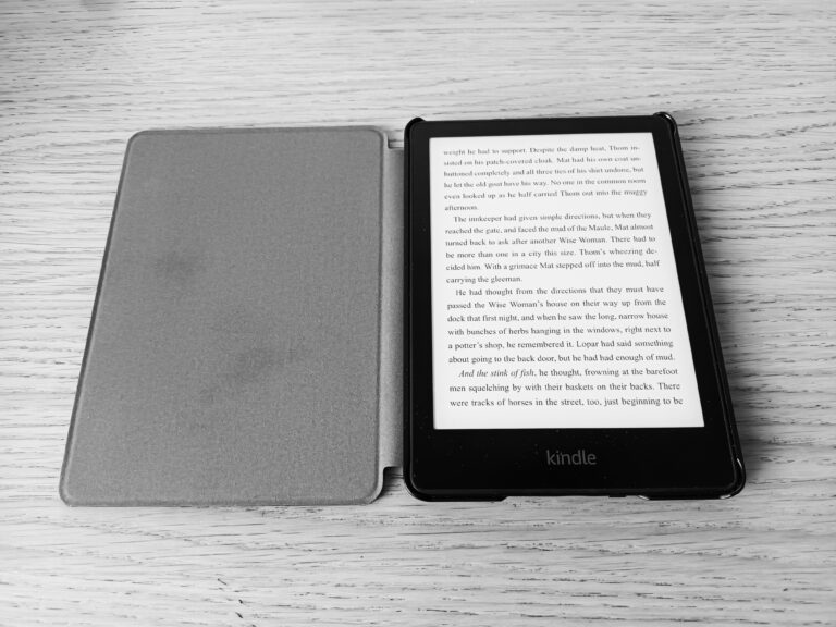 E-czytnik Kindle z otwartą okładką leżący na drewnianym stole.